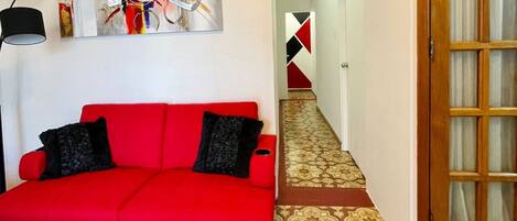 A red sofa with black cushions, a patterned carpet, and a wooden door with glass panels.