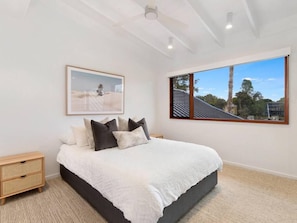 A bedroom with a bed, a nightstand, a framed picture, and a window with a view of trees and a building. - South Straddie Retreat by Laguna Pacific (South Stradbroke)