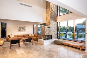 Uma sala de estar moderna com lareira de pedra, sofá modular e grandes janelas com vista para a água.