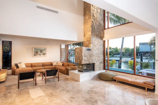 A modern living room with a stone fireplace, a sectional sofa, and large windows overlooking a water body.