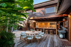 A modern outdoor kitchen with a bar area, wooden deck, and wicker furniture. - South Straddie Retreat by Laguna Pacific (South Stradbroke)