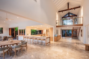 A spacious kitchen with a central island, a dining area with a round table and chairs, and a view of the outdoors through large windows.