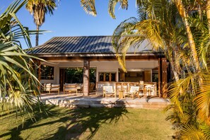 A modern house with a covered patio, outdoor seating, and lush tropical vegetation.