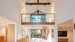 A spacious interior with a high ceiling, a mezzanine level, and a staircase leading to an upper floor. - Quiet Island Paradise! (South Stradbroke)