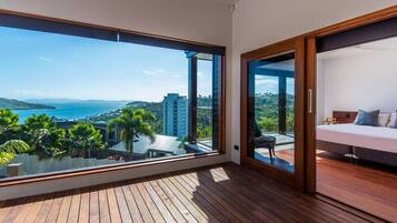 A balcony with a wooden floor and a large window offering a view of the sea and surrounding buildings.