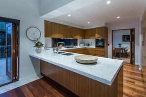A modern kitchen with a central island, wooden cabinets, and a large window. - Horizons - Hamilton Island (Whitsundays)