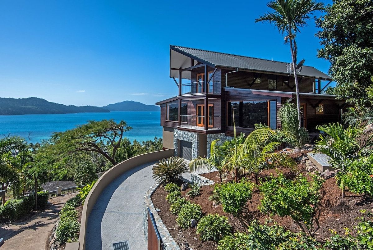 A modern two-story house with a balcony overlooking a coastal landscape.