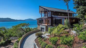 A modern two-story house with a balcony overlooking a coastal landscape.