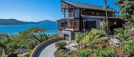 A modern two-story house with a balcony overlooking a coastal landscape.