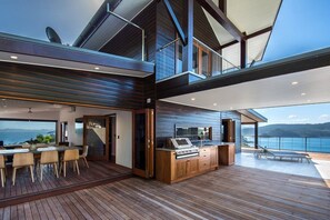 A modern kitchen with a central island, a dining area with a table and chairs, and a view of the ocean. - Horizons - Hamilton Island (Whitsundays)