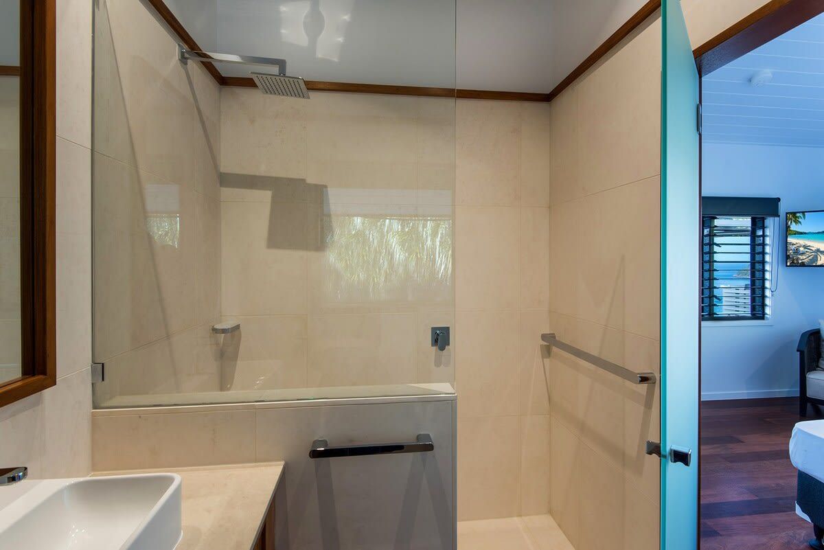 A modern bathroom with a glass shower enclosure, a white sink, and a door leading to another room.