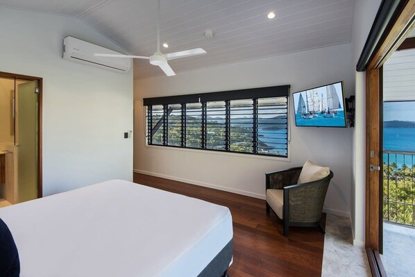 A bedroom with a bed, a chair, a TV, and a large window with a view of the sea. - Horizons - Hamilton Island (Whitsundays)