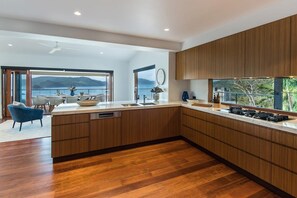 A modern kitchen with wooden cabinets, a large island, and a view of the outdoors. - Horizons - Hamilton Island (Whitsundays)