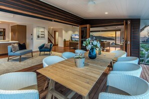 A modern dining area with a wooden table and wicker chairs, a vase with flowers, and a view of the outdoors. - Horizons - Hamilton Island (Whitsundays)
