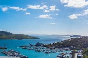A marina with boats docked, a building with a sloped roof, and a hilly landscape in the background. - Horizons - Hamilton Island (Whitsundays)