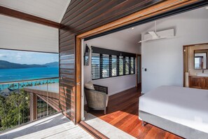 A bedroom with a large bed, a view of the ocean, and a balcony with a railing.