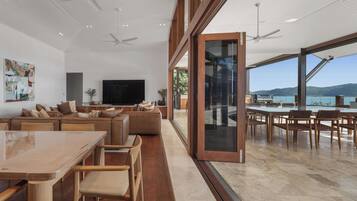 A spacious living area with a large TV, comfortable seating, and a view of the sea.