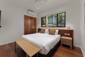 A bedroom with a bed, bedside tables, a bench, a window with a view, and a ceiling fan.