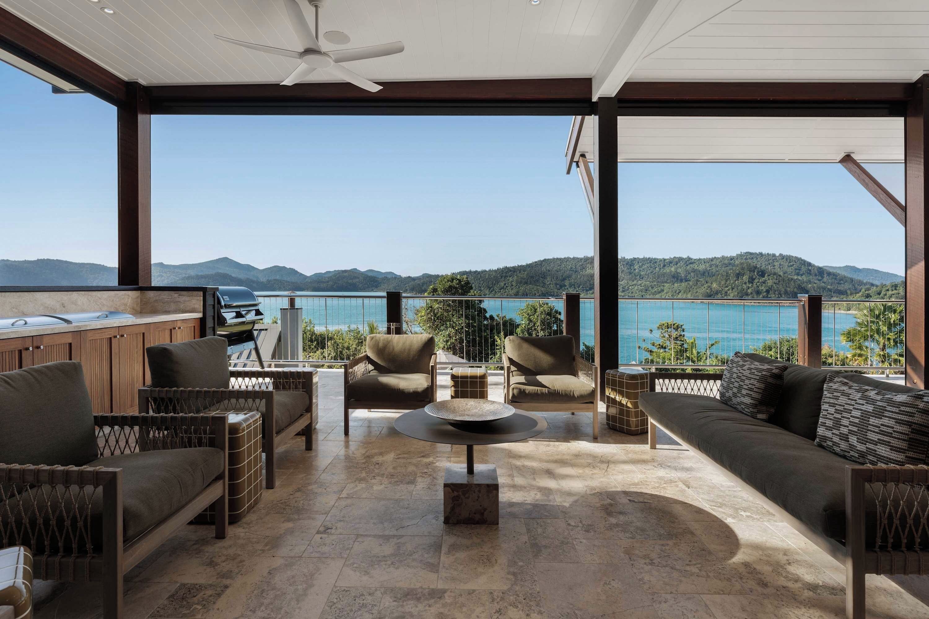 A spacious balcony with a view of the sea and mountains, furnished with a sofa, chairs, and a table.