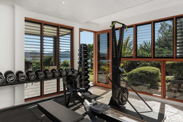 Un gimnasio con equipo de ejercicio, una banca y ventanas amplias con vistas al exterior.