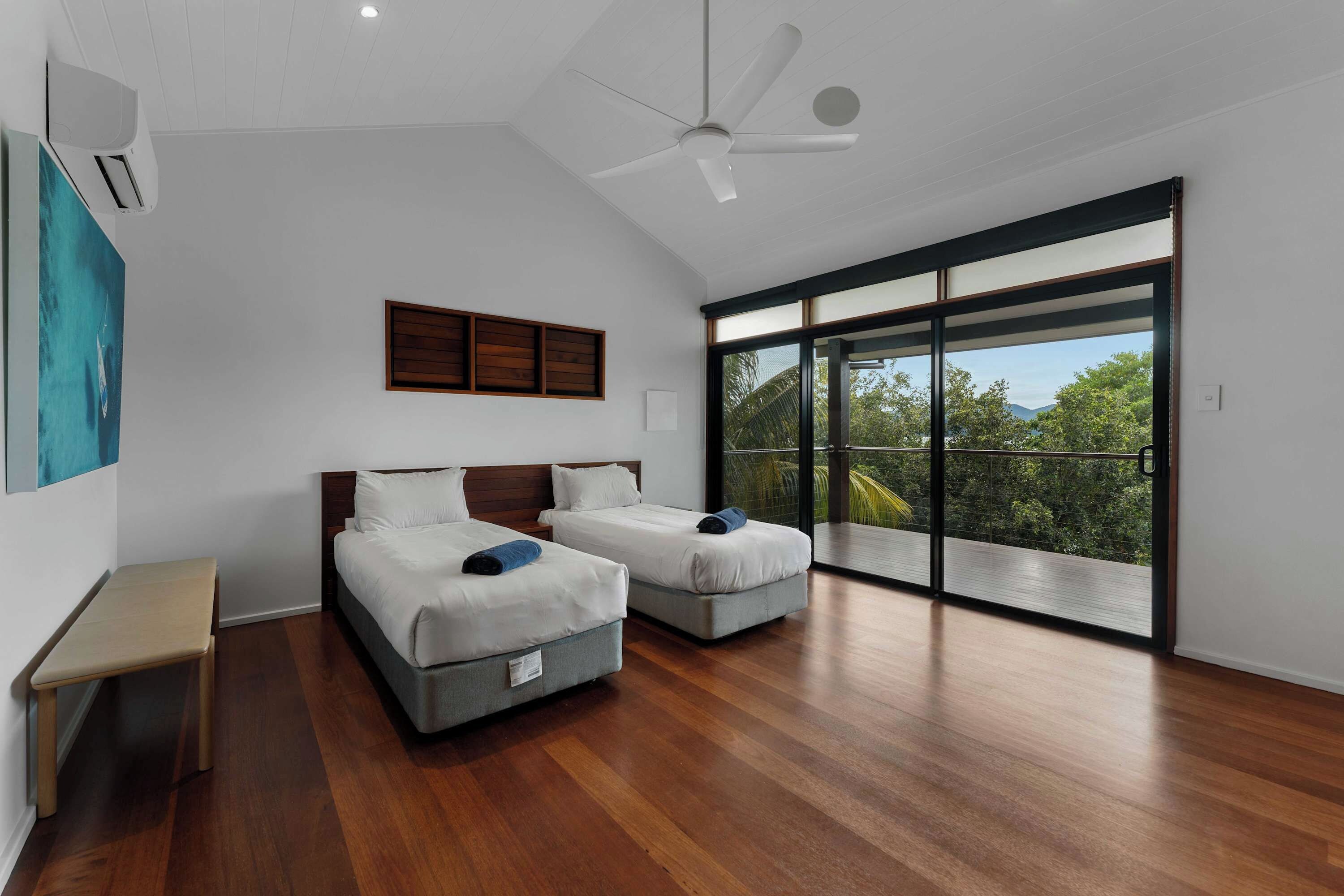 A modern bedroom with two beds, a ceiling fan, and a large sliding glass door leading to a balcony.
