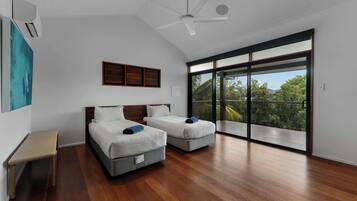A modern bedroom with two beds, a ceiling fan, and a large sliding glass door leading to a balcony.