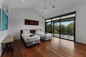 A modern bedroom with two beds, a ceiling fan, and a large sliding glass door leading to a balcony. - Papillon - Hamilton Island (Whitsundays)