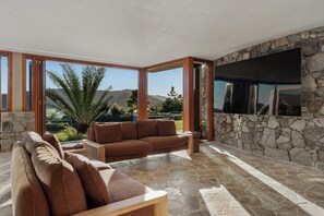 A modern living room with a stone wall, large windows, and a flat-screen TV. - Papillon - Hamilton Island (Whitsundays)