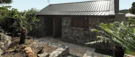 A stone building with a metal roof, a stone staircase, and a small garden area with plants.