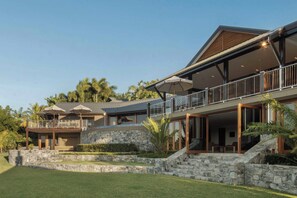 A modern two-story house with a stone retaining wall, a covered outdoor seating area, and a large balcony. - Papillon - Hamilton Island (Whitsundays)