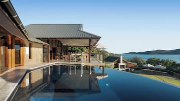 A modern house with a swimming pool, a covered patio, and a view of the water.