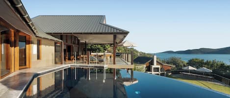 Une maison moderne dotée d’une piscine, d’un patio couvert et offrant une vue sur l’eau.