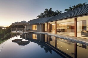 A modern house with a glass-enclosed swimming pool, a balcony with umbrellas, and a view of the surrounding landscape. - Papillon - Hamilton Island (Whitsundays)