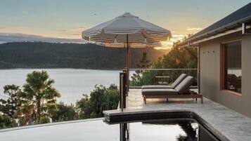 A poolside area with a view of the water, a lounge chair, and a striped umbrella.