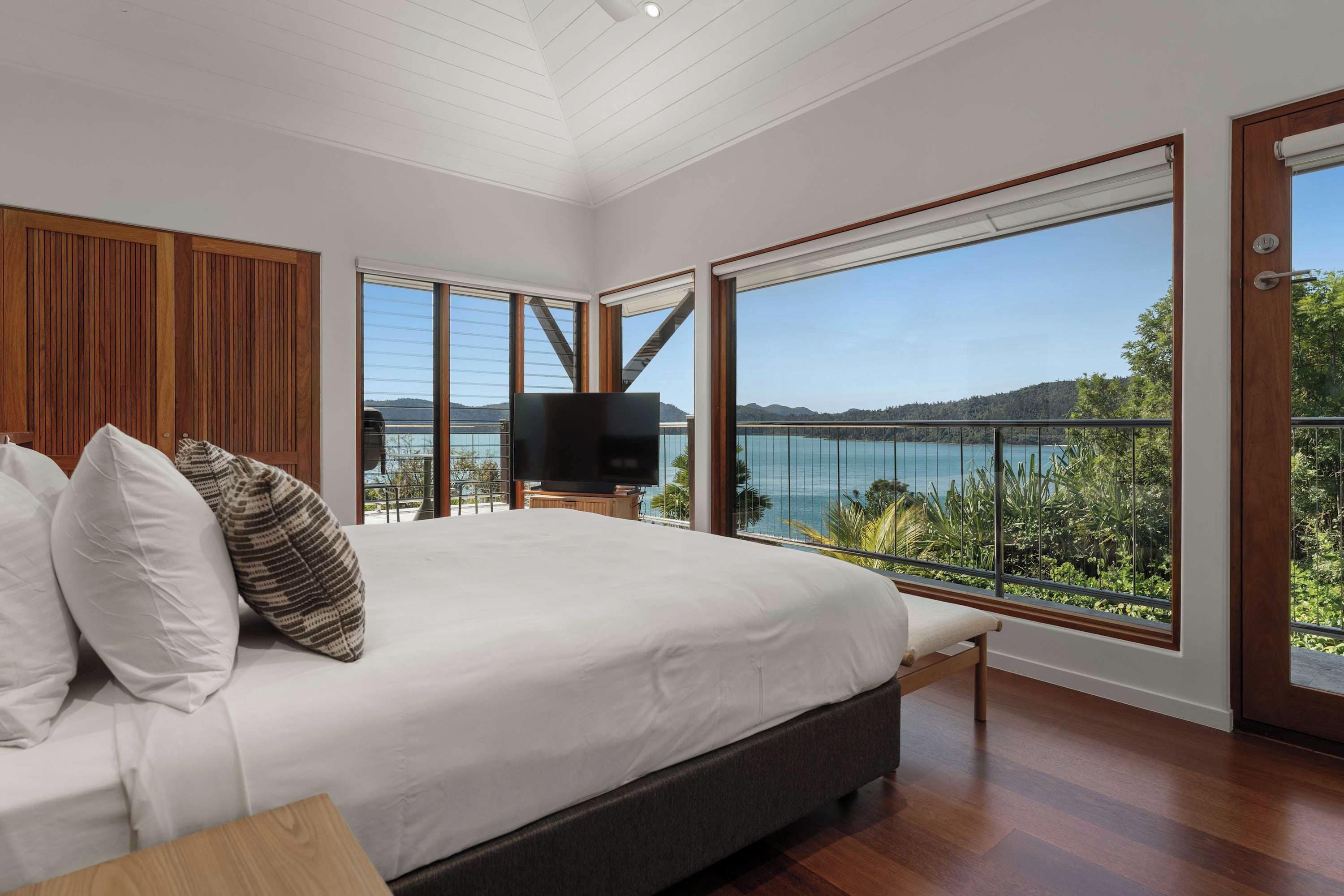 A bedroom with a large bed, a television, and a balcony with a view of the sea.