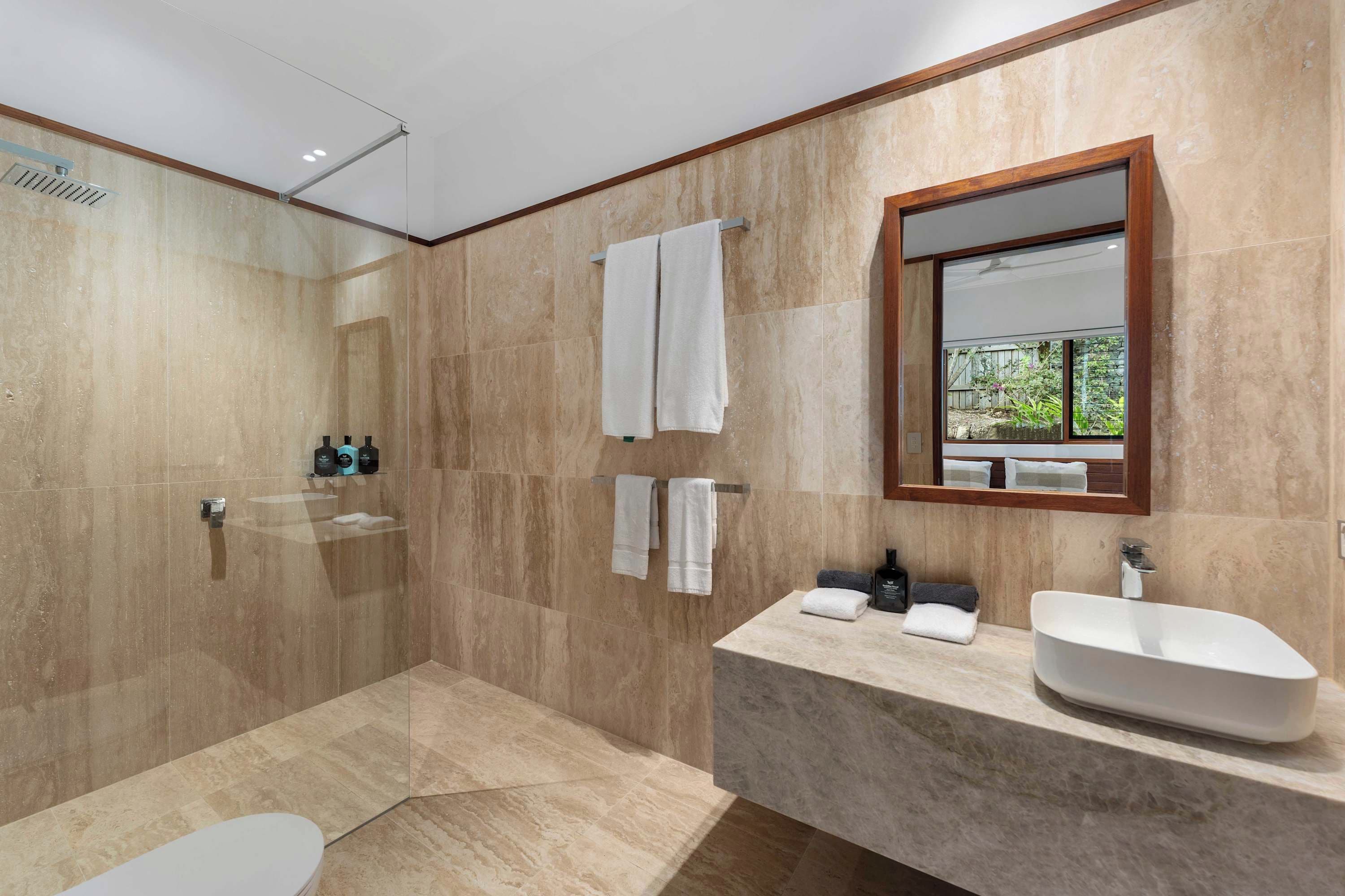Ein modernes Badezimmer mit einer gläsernen Dusche, einem großzügigen Waschtisch mit Aufsatzbecken und einem Fenster mit Blick ins Freie.