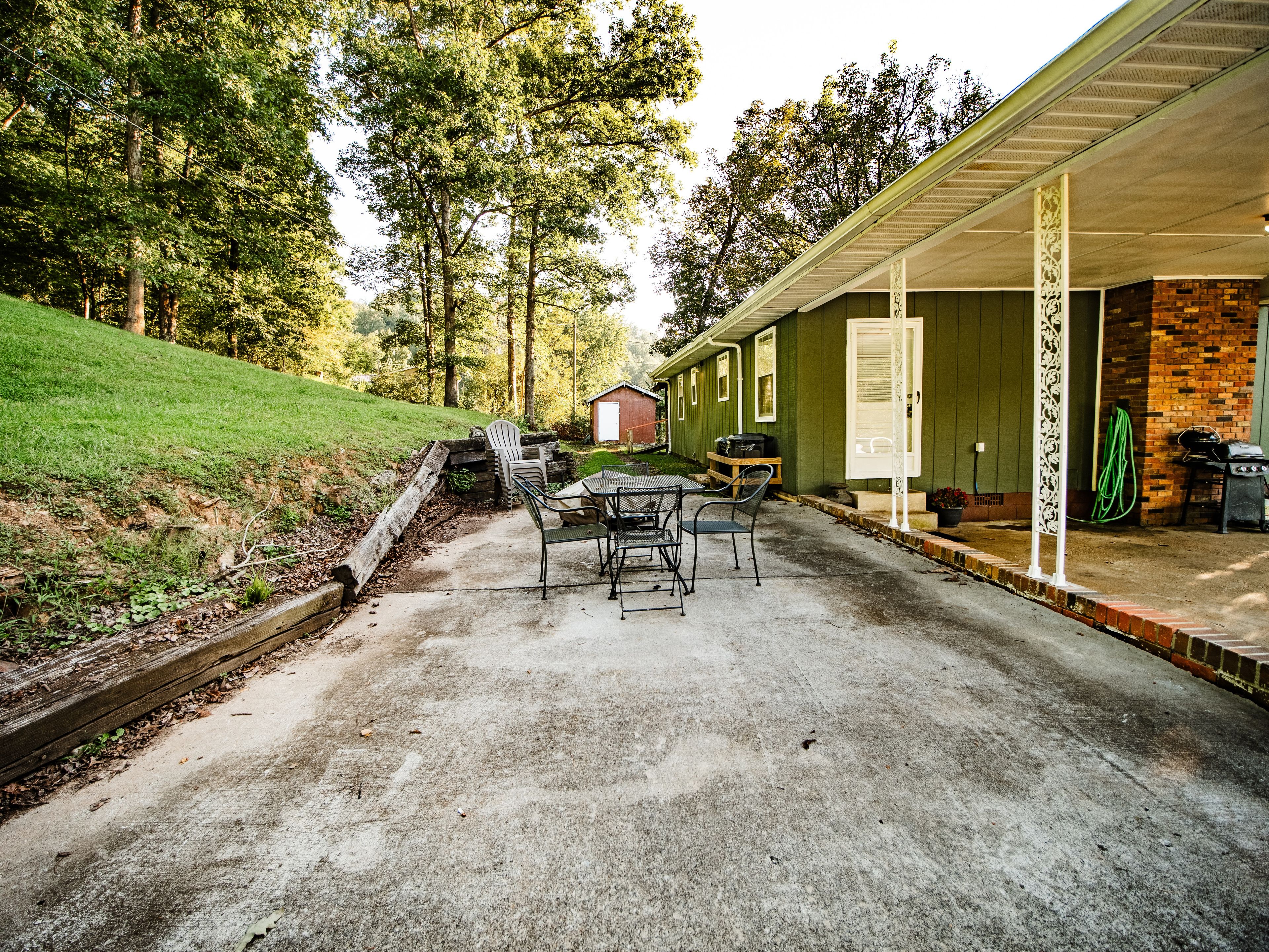 A patio area with a table and chairs, a barbecue grill, and a covered porch with a brick wall.