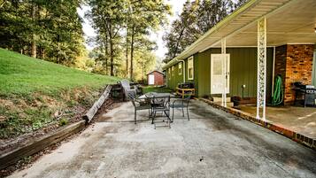 A patio area with a table and chairs, a barbecue grill, and a covered porch with a brick wall.
