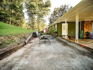 A patio area with a table and chairs, a barbecue grill, and a covered porch with a brick wall.