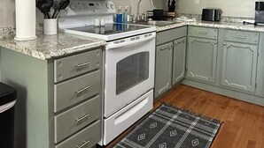 A kitchen with light green cabinets, a white stove, and a granite countertop. - Low Key Living Hideaway (Lavalette)