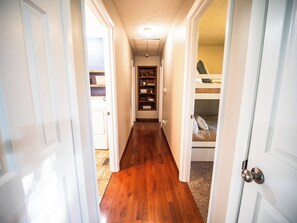 A hallway with wooden flooring, a built-in bookshelf, and a bunk bed.