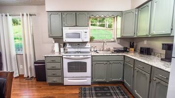 A kitchen with green cabinets, a microwave, stove, and a window with a view of greenery.