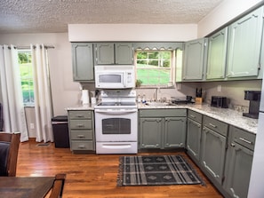 Une cuisine avec des meubles de couleur verte, un four à micro-ondes, une cuisinière et une fenêtre donnant sur un paysage verdoyant.