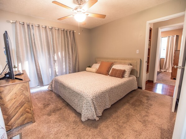 A bedroom with a bed, a ceiling fan, a desk, and a mirror.