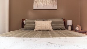 Una cama con una colcha estampada, dos almohadas, una lámpara de noche y un pequeño objeto decorativo sobre una mesita de noche.