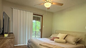 A bedroom with a bed, a ceiling fan, a TV on a wooden dresser, and a sliding glass door to a balcony. - Low Key Living Hideaway (Lavalette)