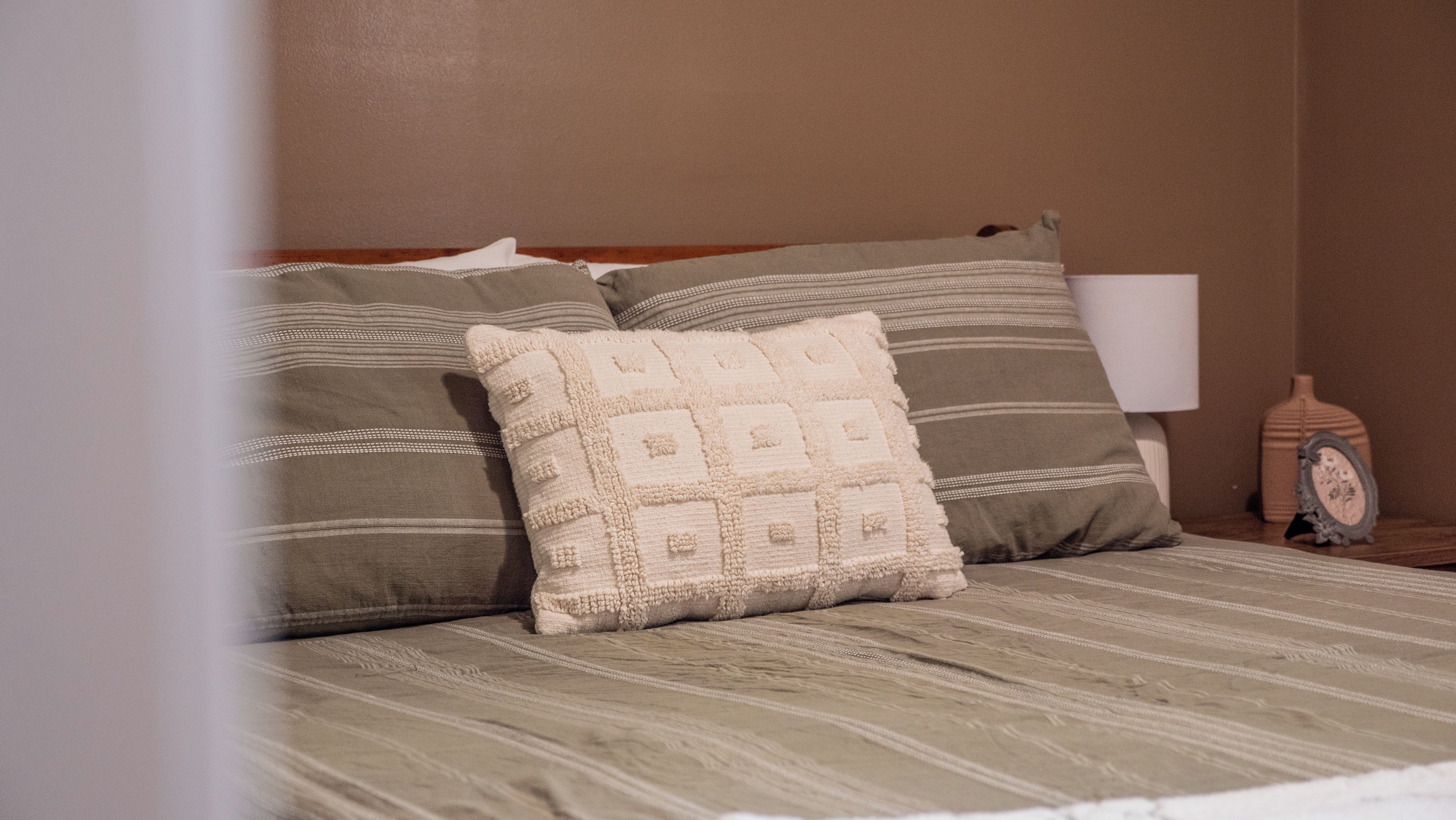 A bed with striped bedding and two pillows, one with a geometric pattern and the other with stripes.