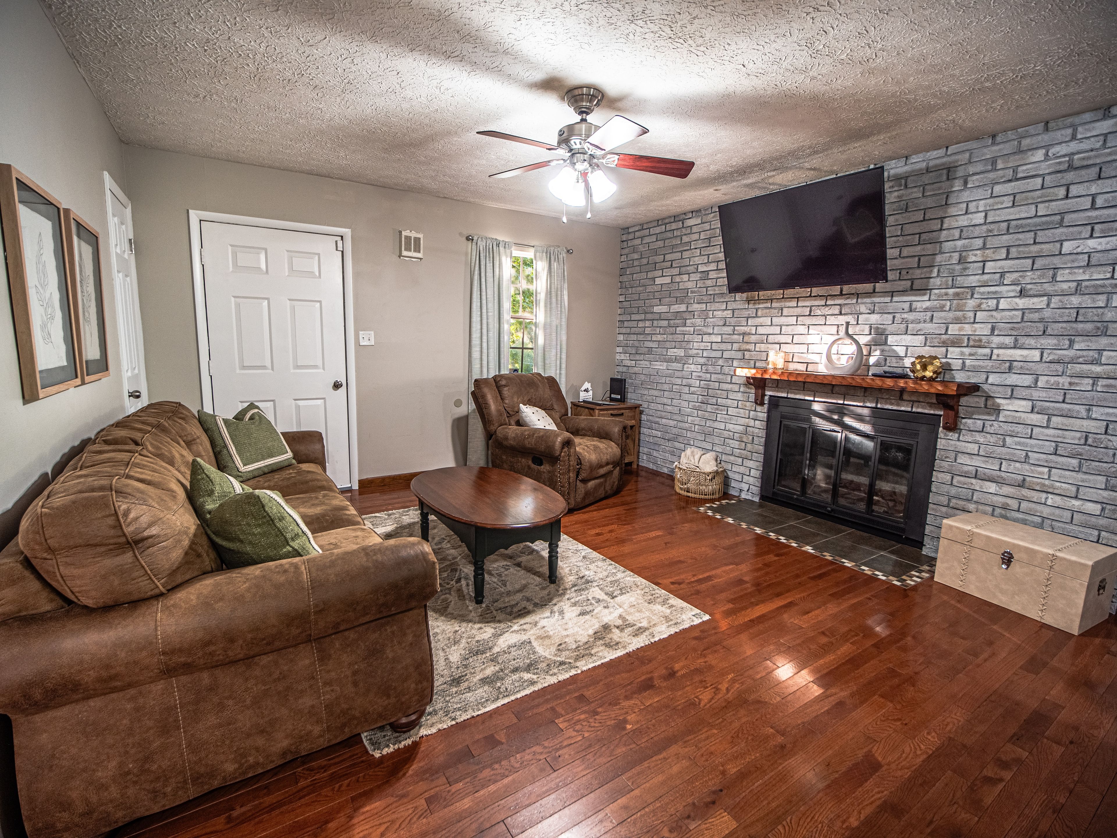 A living room with a fireplace, a sofa, a recliner, and a television mounted on the wall.