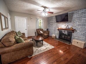 A living room with a fireplace, a sofa, a recliner, and a television mounted on the wall.