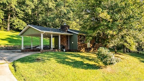 A small brick building with a covered porch, surrounded by lush greenery and trees.